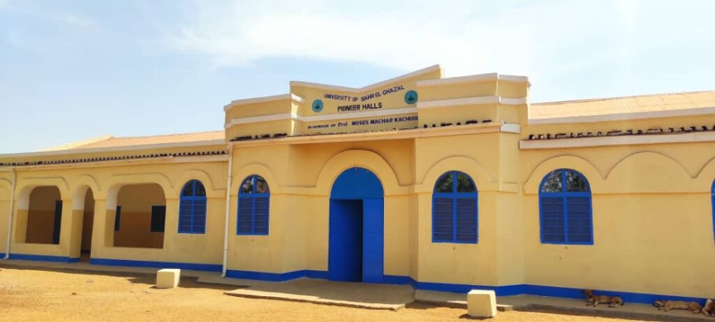 The "Pioneer Halls" building at the University of Bahr el Ghazel, a yellow and blue structure named in honor of Prof. Moyses Machar Kachuol, stands empty under a clear sky during a staff strike in Wau.
