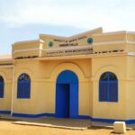 The "Pioneer Halls" building at the University of Bahr el Ghazel, a yellow and blue structure named in honor of Prof. Moyses Machar Kachuol, stands empty under a clear sky during a staff strike in Wau.
